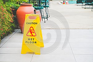 Yellow caution wet floor sign board on floor near swimming pool