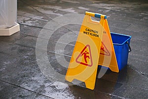 Yellow Caution wet floor sign on wet floor with blue bucket