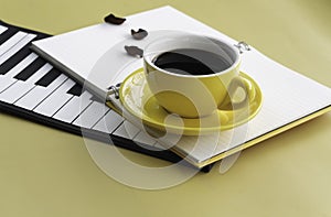 Yellow ceramic cup with black coffee put beside piano pad