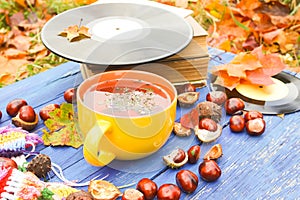 Yellow ceramic cup of herbal tea and vintage vinyl records on aged wooden background with fall autumn leaves and chestnuts