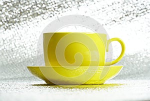 Yellow ceramic glossy cup in saucer on silver background. Template for coffee or tea