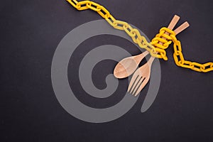 Yellow chain locked around the wooden spoon and fork on black st