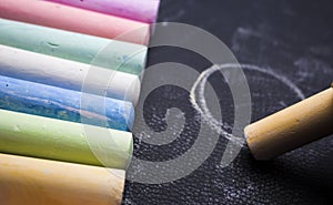 Yellow chalk draws a circle, on a black background with lying colored crayons in a row