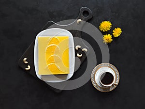 Yellow cheesecake with oranges and cup of coffee on a black background