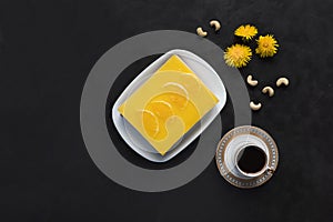 Yellow cheesecake with oranges and cup of coffee on a black background
