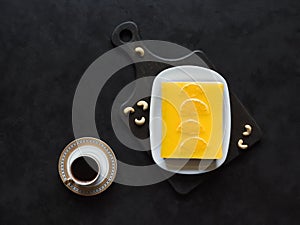 Yellow cheesecake with oranges and cup of coffee on a black background