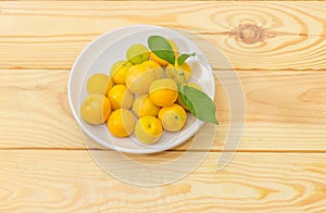 Yellow cherry plums on white saucer on wooden surface