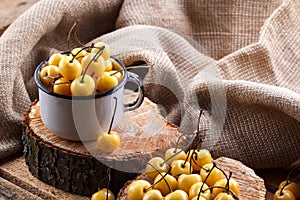 Yellow cherry in a rustic style on a wooden background. Berries of ripe fresh cherries in a cup.