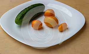 Yellow cherry tomatoes and green cucumber on a white glossy plate in the form of a sad facial expression