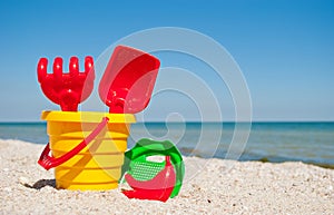 Yellow child pail with a red handle, plastic red spatula and rake, and a plastic green sieve, a red sand form in the form of a ban