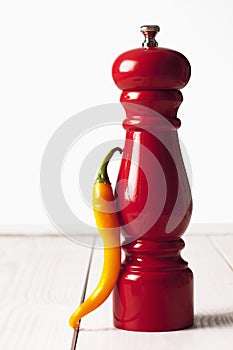 Yellow chili and red pepper grinder on white wooden table