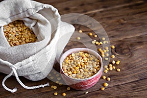 Yellow chopped peas in a clay cup and in an eco bag on a wooden table