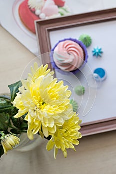 Yellow chrysanthemum in the focus on the background of wooden frame with cupcakes and meringue, flatlay