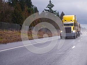 Yellow classic big rig semi truck running on the raining highway