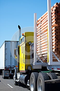 Yellow classic big rig semi truck transports processed round log