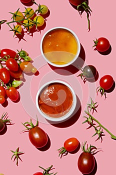 Yellow and classic tomato ketchup sauce and ripe red raw tomatoes on pink colored background, top view