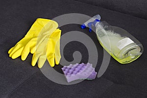 Yellow cleaning gloves, a sponge and a cleanser on the couch screen