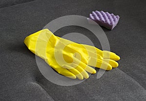 Yellow cleaning gloves and a sponge on the couch, close-up