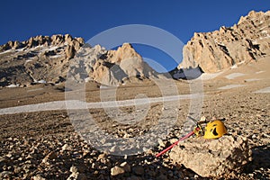 Yellow climbing helmet and red ice axe, lying on a rock in the mountains