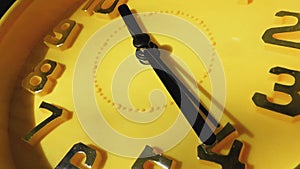 Yellow clock with black arrows running in a circle, close-up.