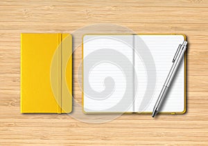 Yellow closed and open lined notebooks with a pen on wooden background