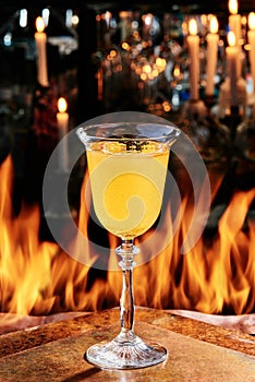 Yellow cocktail in a beautiful goblet glass on copper designer bar counter, the background of real fire. autumn cocktail