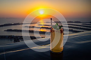 Yellow cocktail on the edge of an infinity pool with a panorama of Dubai Palm during sunset