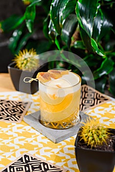 Yellow cocktail with white protein foam in a beautiful old fashion glass, decorated with a mango skewer
