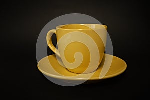 Yellow coffee cup and saucer on a black background.