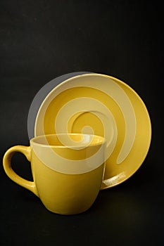 Yellow coffee cup and saucer on a black background.