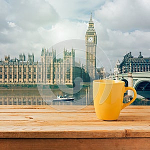 Yellow coffee cup on wooden table over London Big Ben