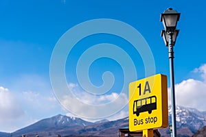 Yellow color bus stop sign with blue sky and snow mountain in background