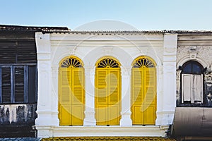 Yellow color wooden arched window on white cement wall in chino Portuguese style at Phuket old town, Thailand