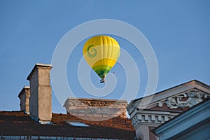 Yellow colorful hot air balloon flying in blue sky over roofs of city