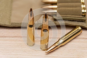 Yellow combat rifle cartridges with bullets in a 7.62 caliber military bandolier on a wooden background.