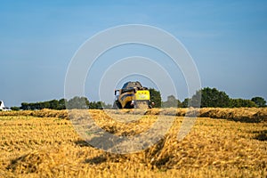 Yellow combine harvester New Holland harvests ripe wheat field. Agriculture in France. Harvesting is the process of