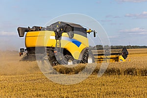 Yellow combine harvester on a wheat field with blue sky