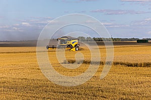 Yellow combine harvester on a wheat field with blue sky