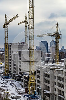 Yellow construction building cranes in winter on the construction site of a large residential modern high-rise building at the