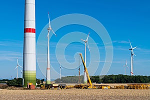 A yellow construction crane is assembling a metal structure in front of windmills