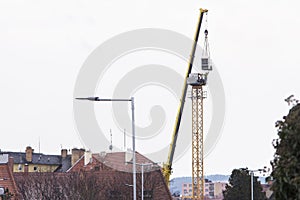 Yellow construction crane being assembled using car crane. Silhouette of a worker reaching for a crain cab to attach it. Construct