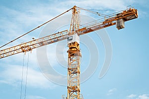 Yellow construction crane with cabin against blue sky. Lifting of cargo. Construction machinery concept, modern technology