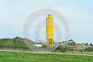 A yellow container for concrete mixers and an elevator for loading dump trucks