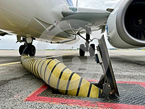 Yellow cooling airconditioning hose or pipe out of tarmac ground point with red lines connected to underside of airplane