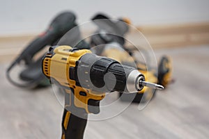 Yellow cordless drill with additional power tools in the background. Construction work, home improvement, mechanical tasks and