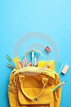 Yellow corduroy backpack overflowing with colorful school supplies, set against a striking blue backdrop. Ideal for educational