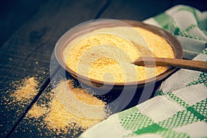 Yellow corn flour in a ceramic bowl on a rustic wooden table. In