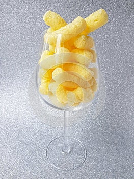 Yellow corn sticks in a transparent glass on a silver background.
