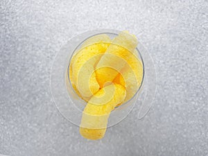 Yellow corn sticks in a transparent glass on a silver background.