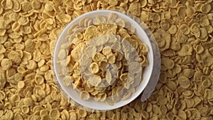 Yellow cornflakes in a white bowl and with flakes in the background are slowly rotating. Concept of healthy food -